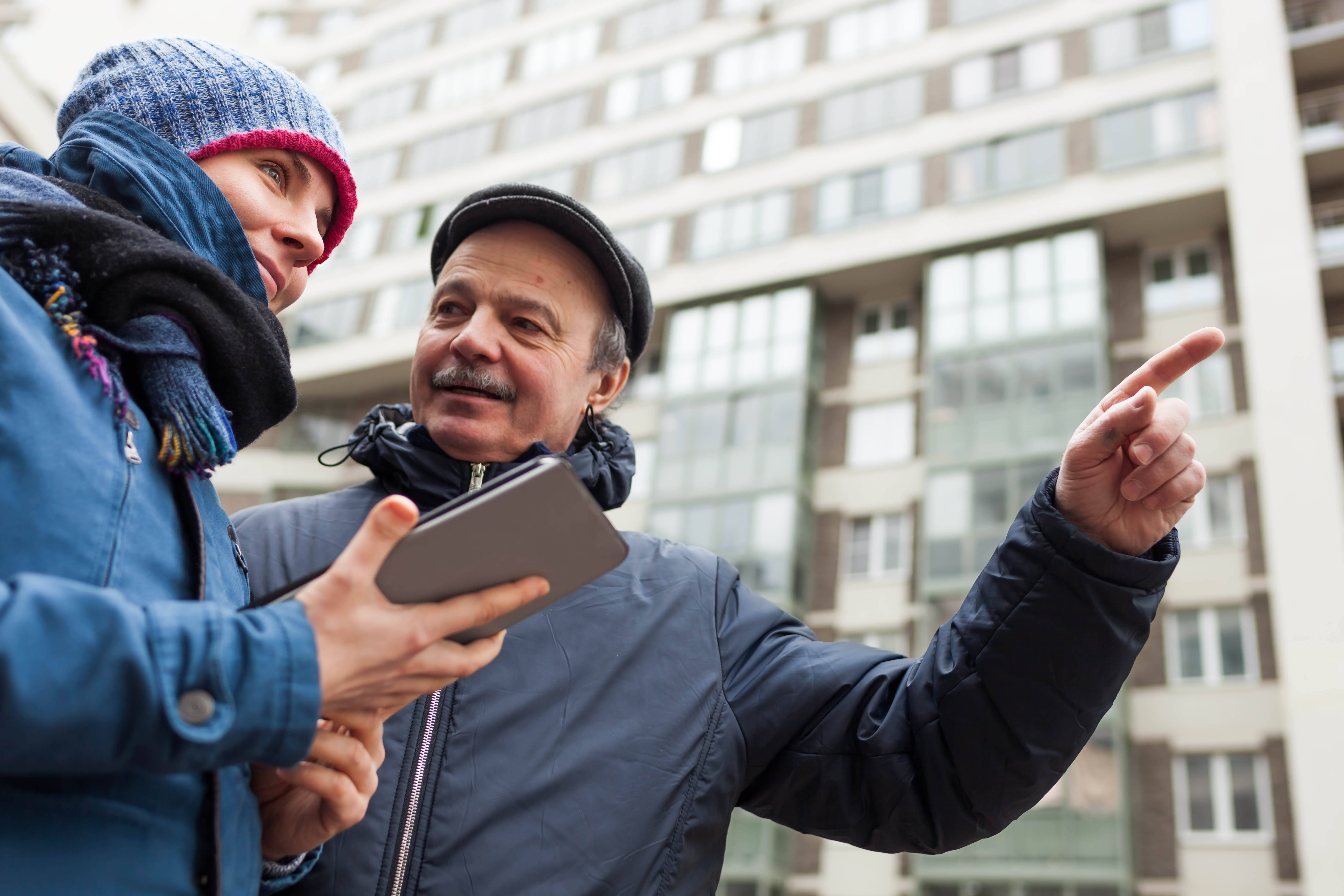 Older man on the street giving a younger woman - who's holding her phone out - directions